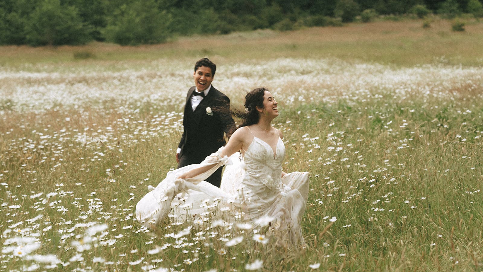 bride and groom joyfully running around field of daises