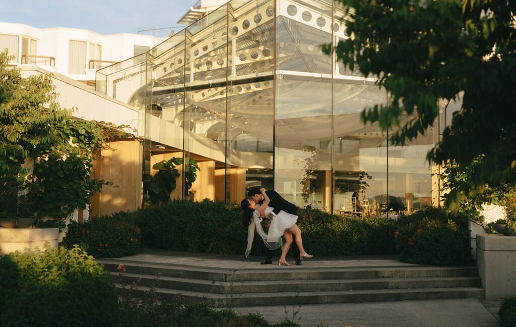 wedding couple kissing in front of large windows reflecting the sunset on the water of victoria downtown waterfront