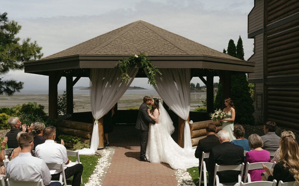 Couple sharing their first kiss at ceremony under gazebo in front of the ocean at Tigh-Na-Mara Resort