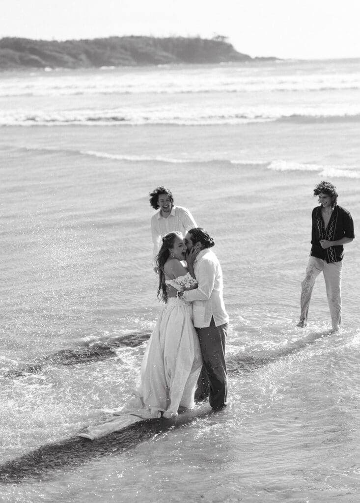 A black and white image shows newlyweds sharing their first kiss after their elopement ceremony at pacific sands beach resort tofino bc