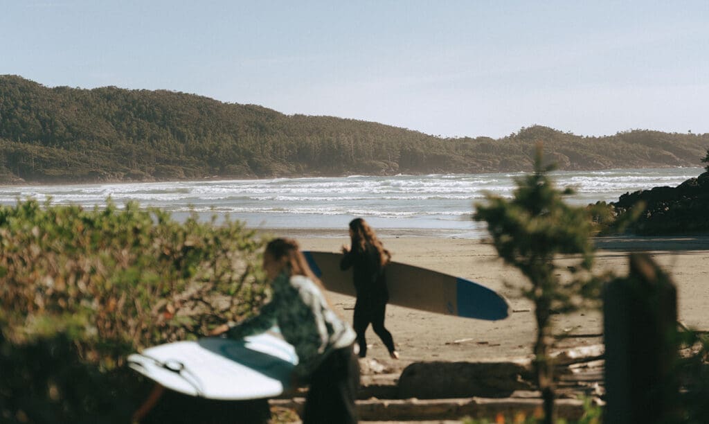 Newlyweds carry their surf boards across the sand following their pacific sands beach resort wedding