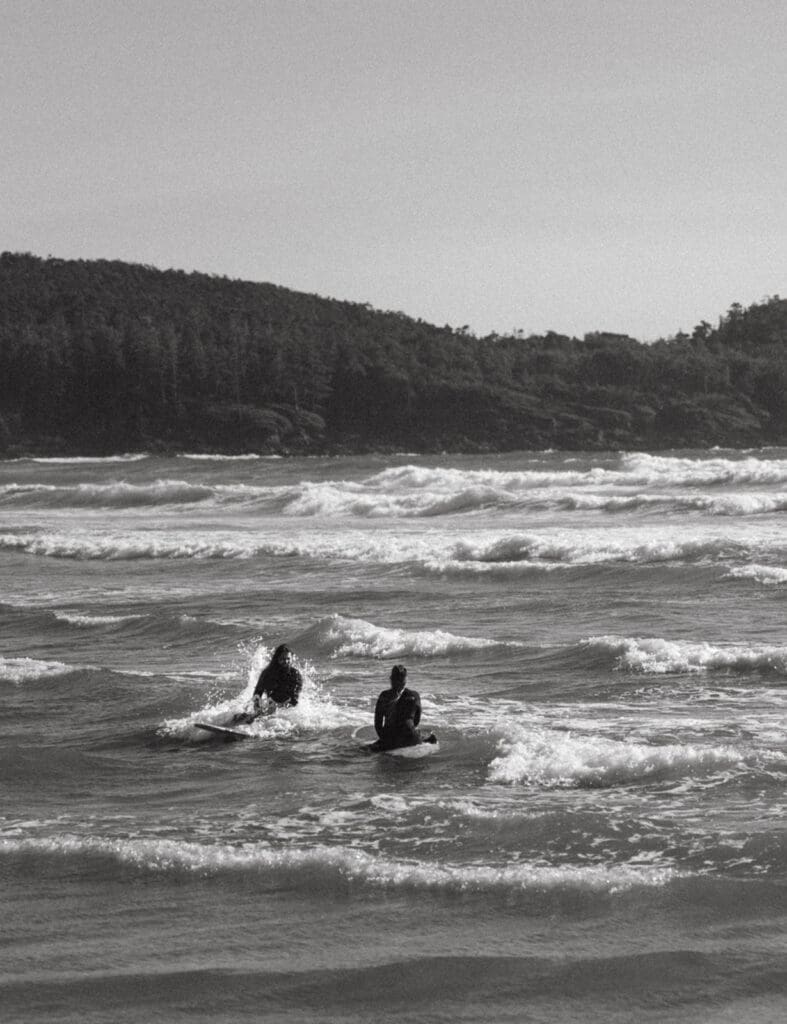 A b+w photo shows newlyweds sharing a surf together following their elopement ceremony at pacific sands beach resort tofino bc