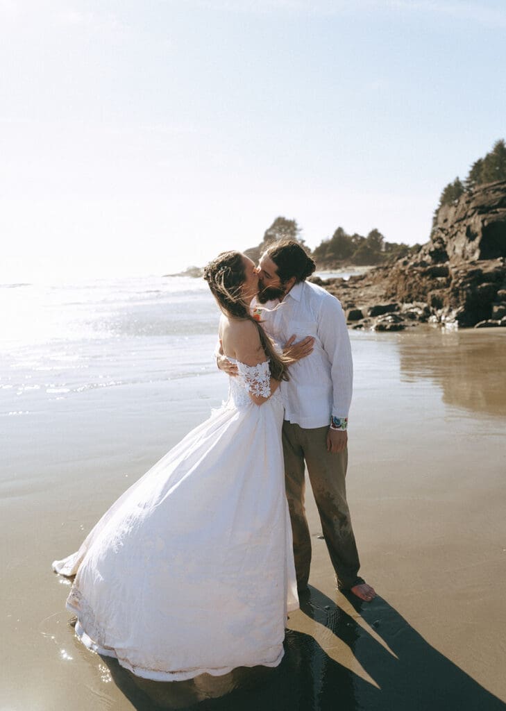A bride and groom in their wedding attire share a kiss following their Tofino elopement on the beach 