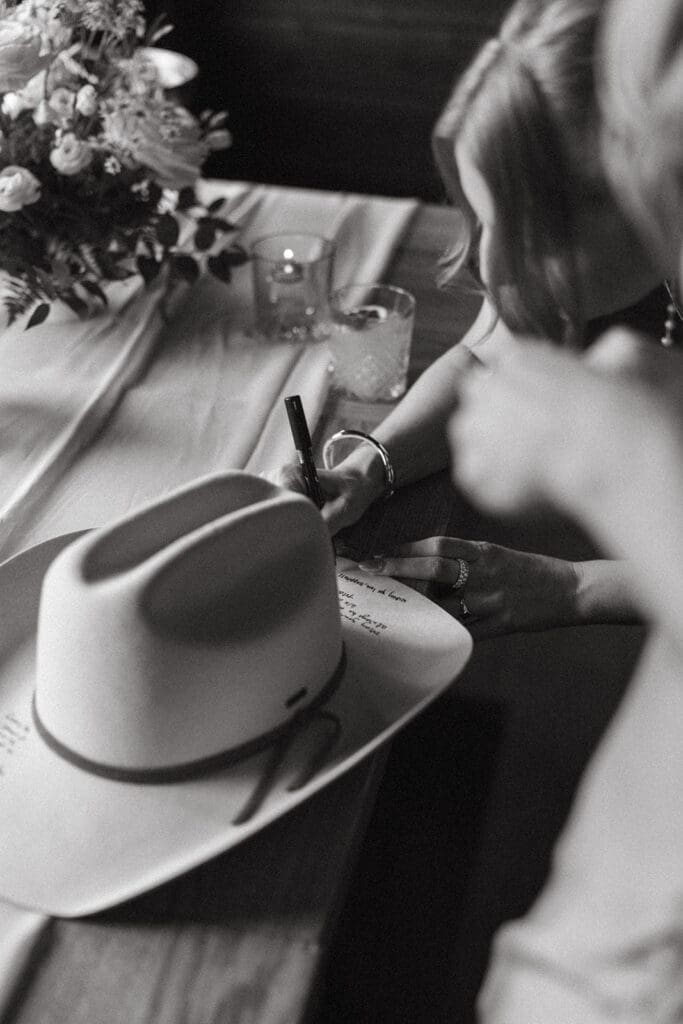 A guest signs a cowboy hat in a black and white photo taken at a banff wedding reception at Bluebird Restaurant