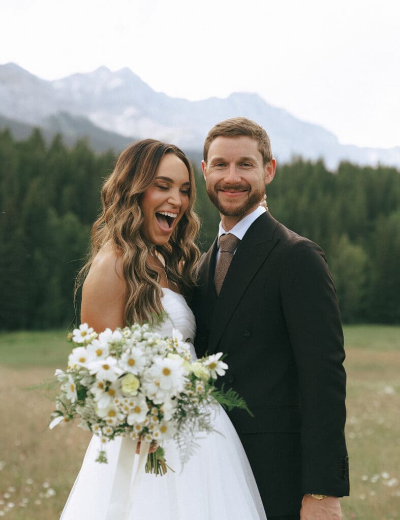 A bride holds a bouquet of white florals as she stands next to her new husband at their Banff Wedding 