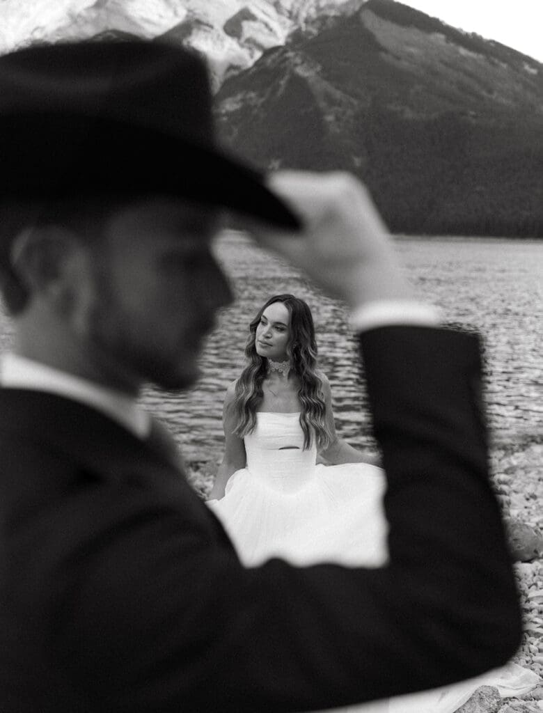 A black and white bridal portrait taken at Lake Moraine showcases a groom in a cowboy hat and a bride in a strapless gown before their destination Banff wedding 