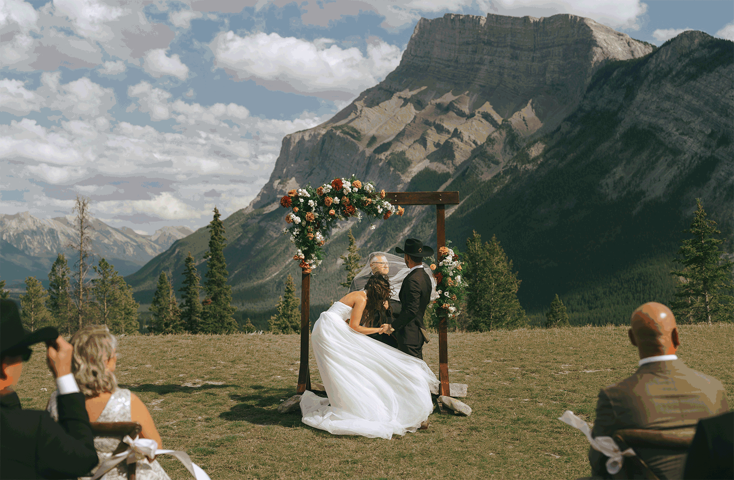 A GIF captures a groom fighting his bride's veil against the wind as the couple & guests laugh at a Tunnel Mountain Reservoir wedding 