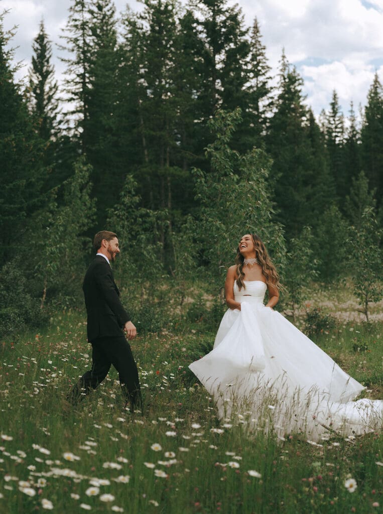 A bride & groom laugh together in a field of flowers before their Banff wedding 