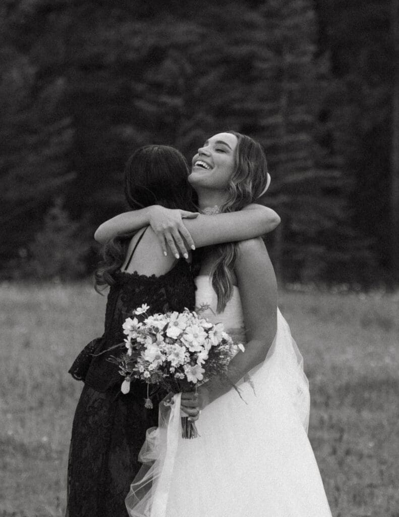 A bride receives a hug from a guest in a black and white photo taken by Alberta wedding photographer, Taylor Dawning Photography