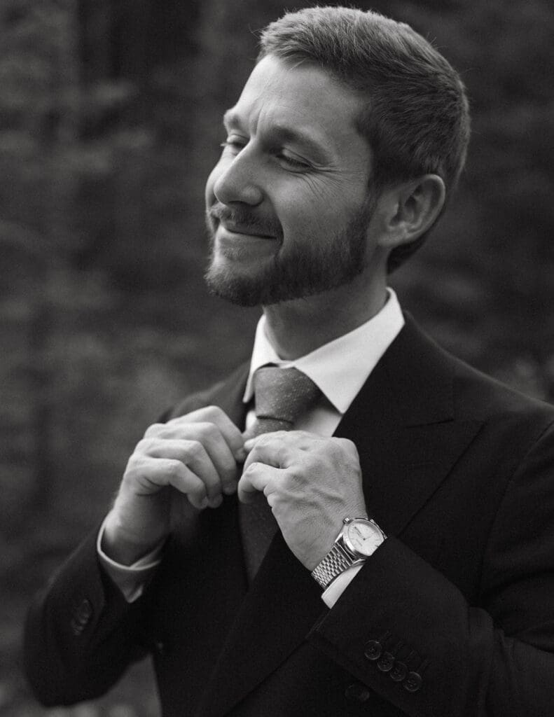 A groom adjusts his tie in a b+w photo taken by Central Alberta wedding photographer, Taylor Dawning 