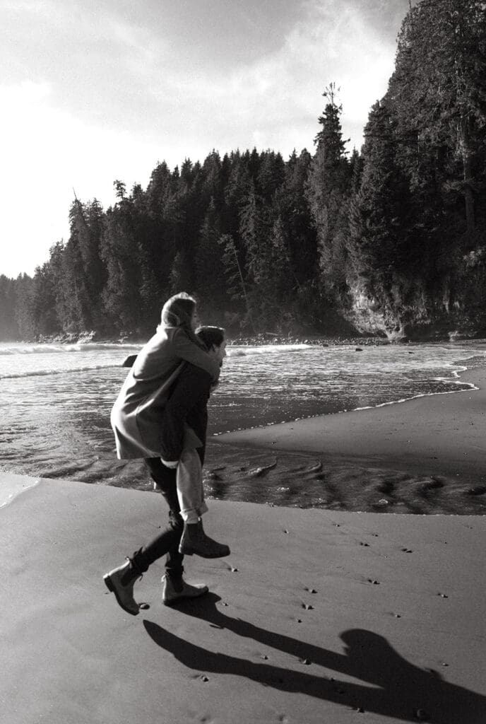 a b+w image of a couple walking along the beach during an engagement photoshoot vancouver island