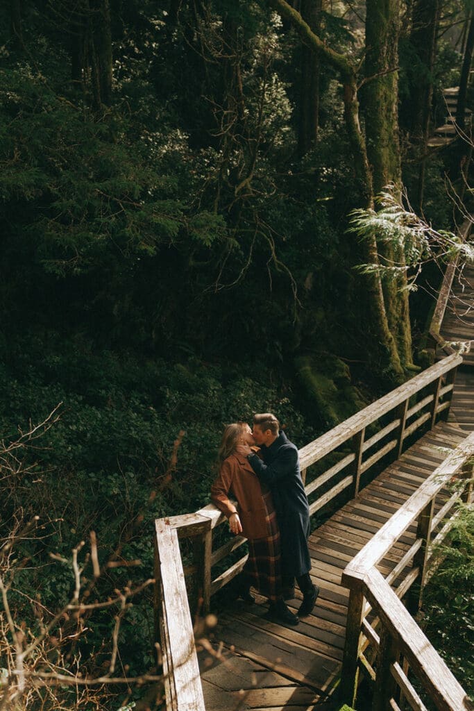 Couple snuggling on Tofino forest boardwalk off of Tonquin Beach, taken by Tofino Wedding Photographer Taylor Dawning