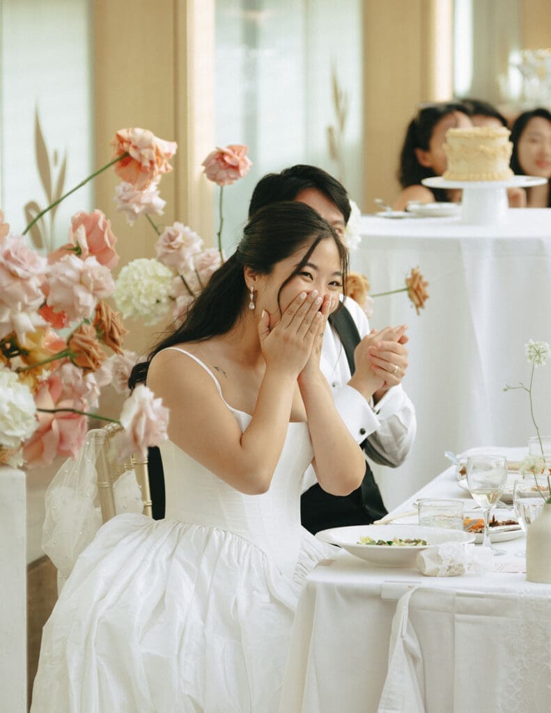 A bride and groom smile while listening to a speech at their laurel point inn wedding reception