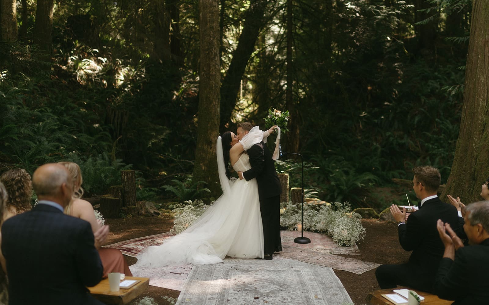 Bride and Groom share first kiss on boho rugs in the forest at their intimate wedding ceremony at Cedar Haven Wedding Venue