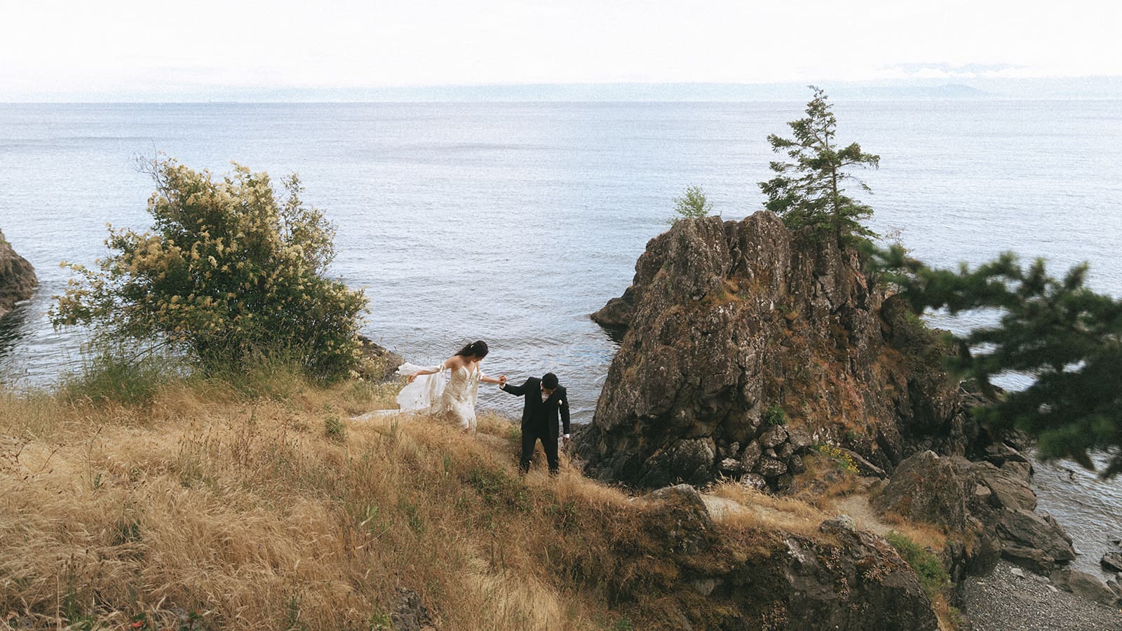 groom helping his bride on a rocky path near the water on the Gulf Islands