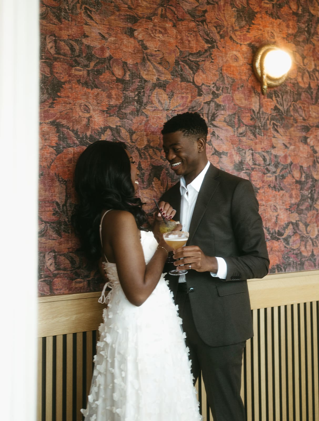 bride and groom leaning against a colourful wallpaper wall while holding drinks inside Downtown Victoria restaurant