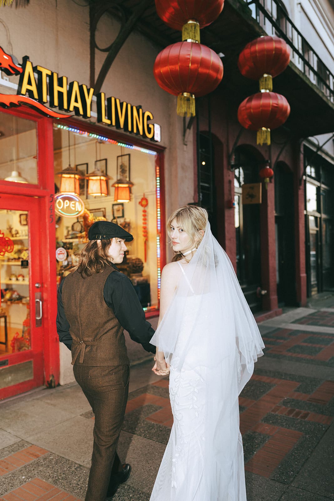 bride and groom holding hands and looking back at the camera while walking through Chinatown in Victoria