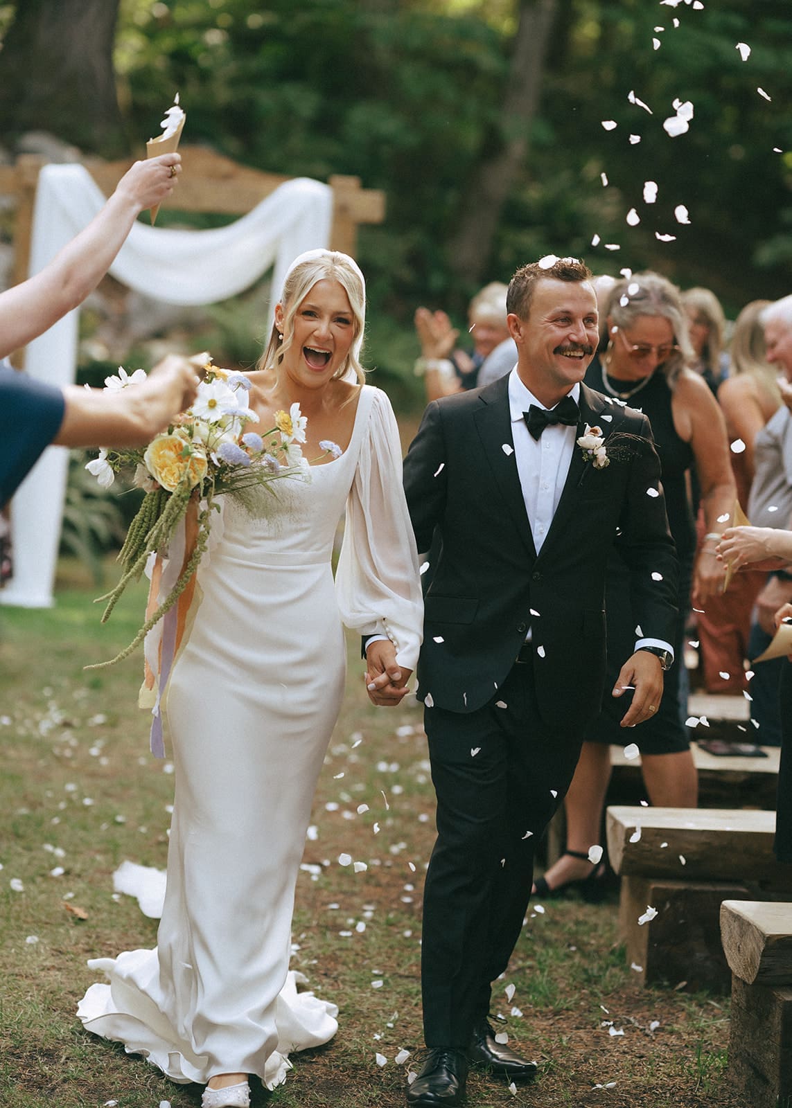 bride and groom exiting ceremony while guests throw flower petals at West Coast River Lodge